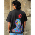 Person wearing a black t-shirt with a colorful graphic design on the back, standing against a stone wall.