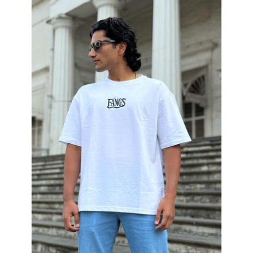 Person wearing a white t-shirt with 'FANGS' logo in front of a classical building.
